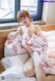 A woman in a white and pink kimono sitting on a bed.