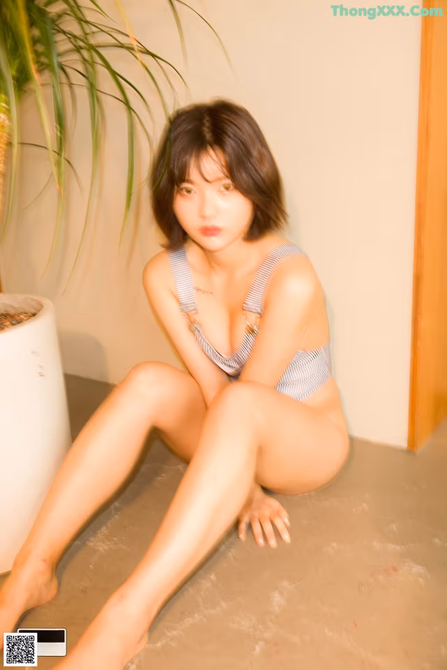 A woman sitting on the floor next to a potted plant.