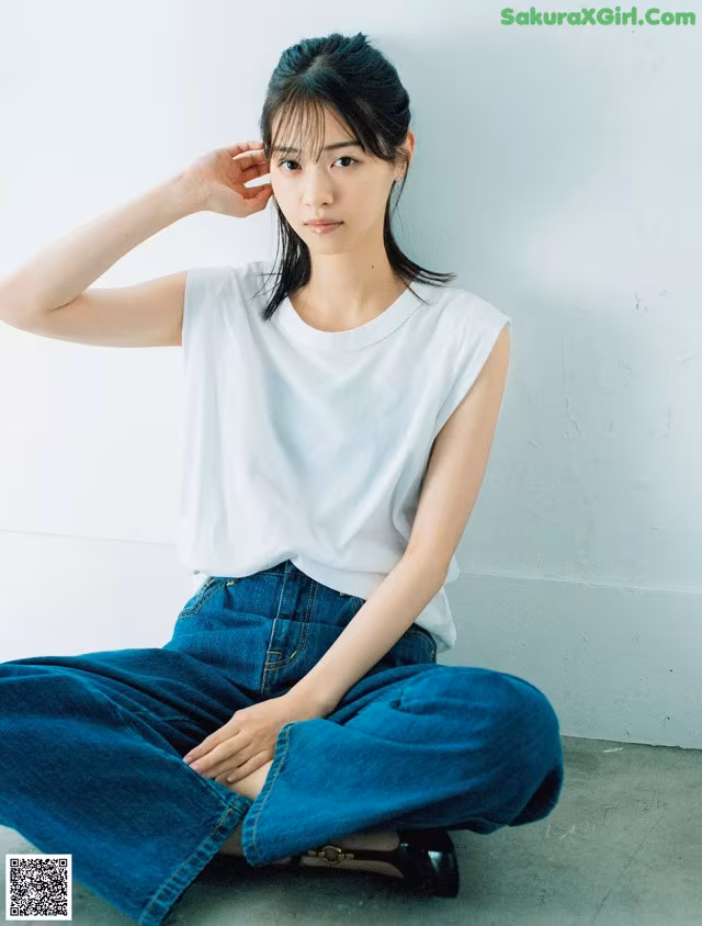 A woman sitting on the floor wearing a white shirt and blue jeans.