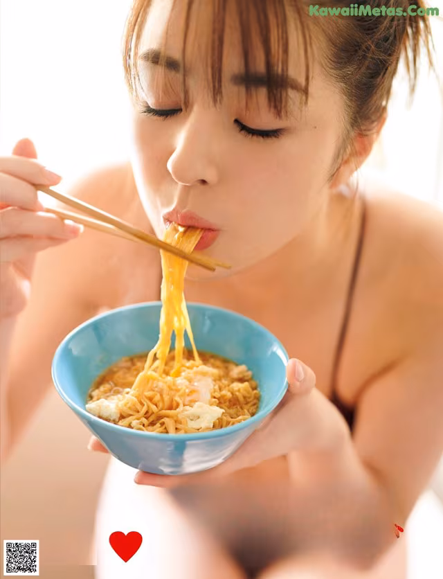 A woman eating a bowl of noodles with chopsticks.