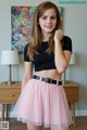 A young woman wearing a black top and a pink skirt.