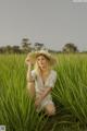 A woman in a white dress and straw hat sitting in tall grass.