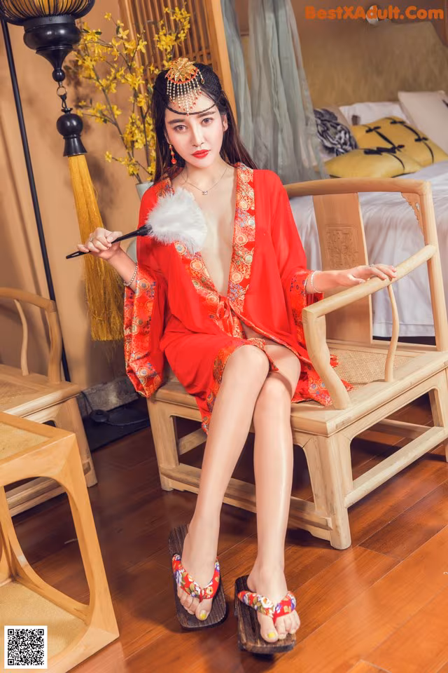 A woman in a red dress sitting on a wooden chair.