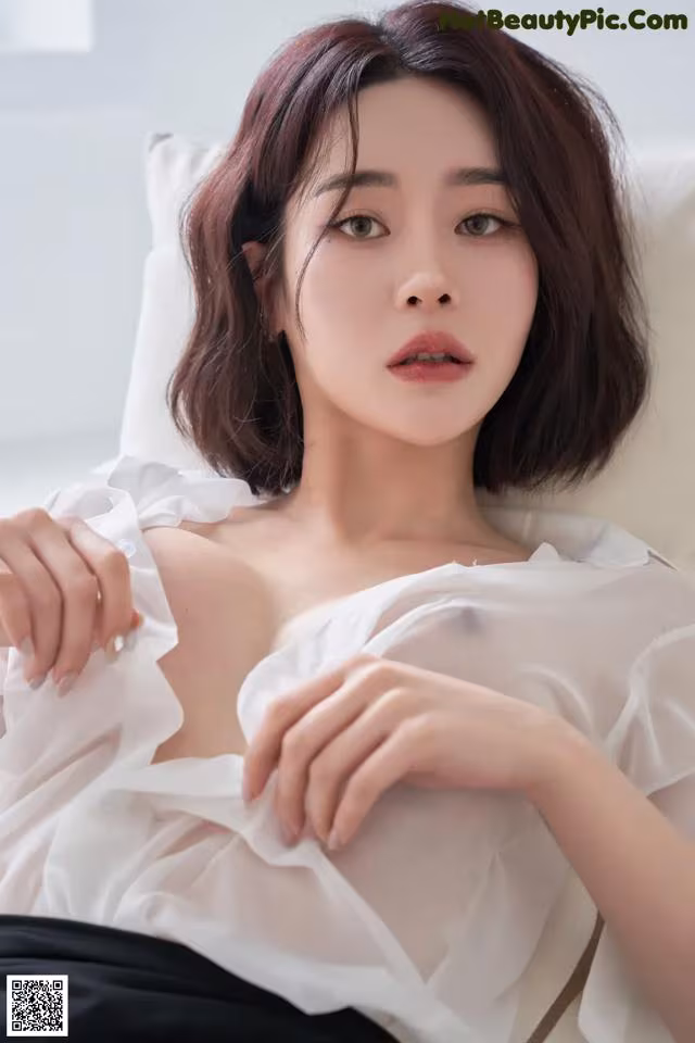 A woman in a white blouse sitting on a white couch.