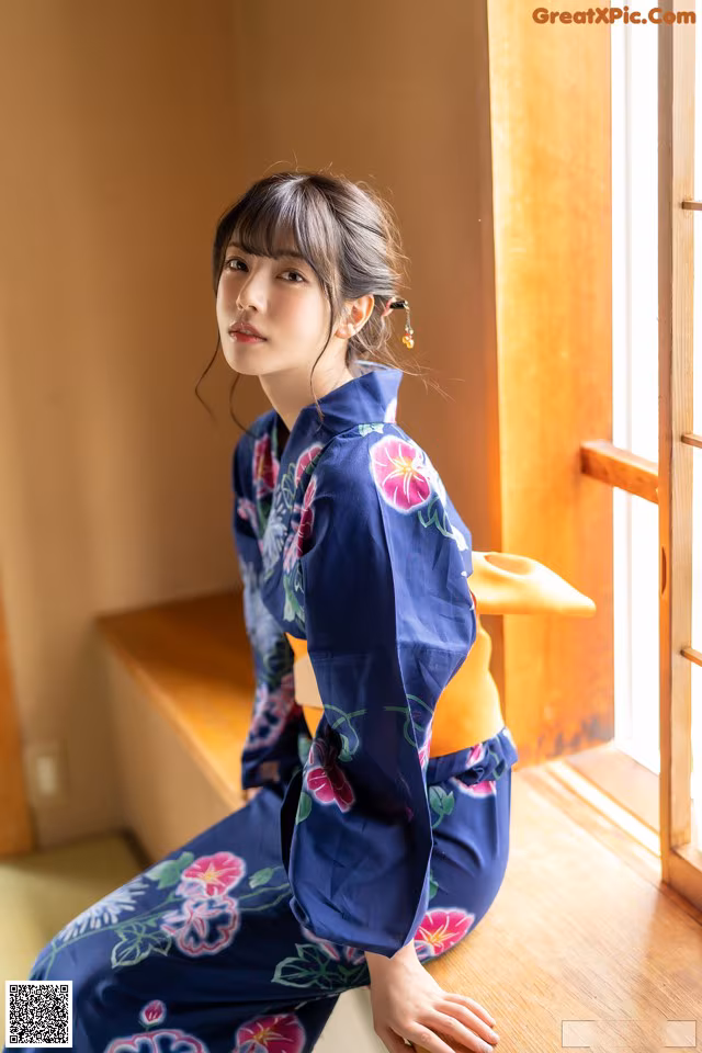 A woman in a blue kimono sitting on a window sill.