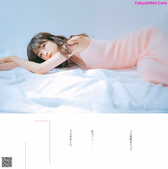 A woman laying on top of a bed in a pink dress.