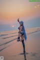 A woman with long blue hair standing on a beach.