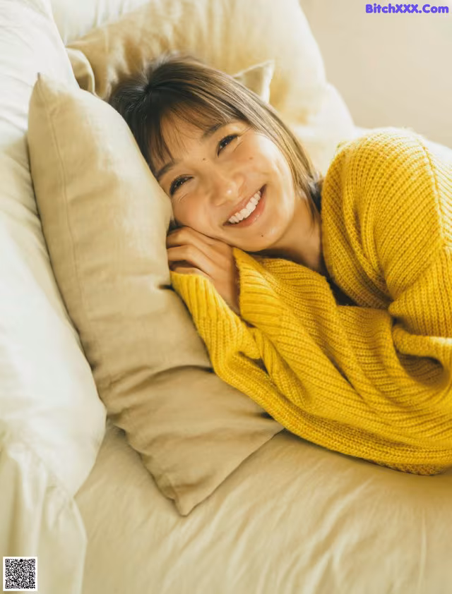A woman laying on a bed with a yellow sweater on.