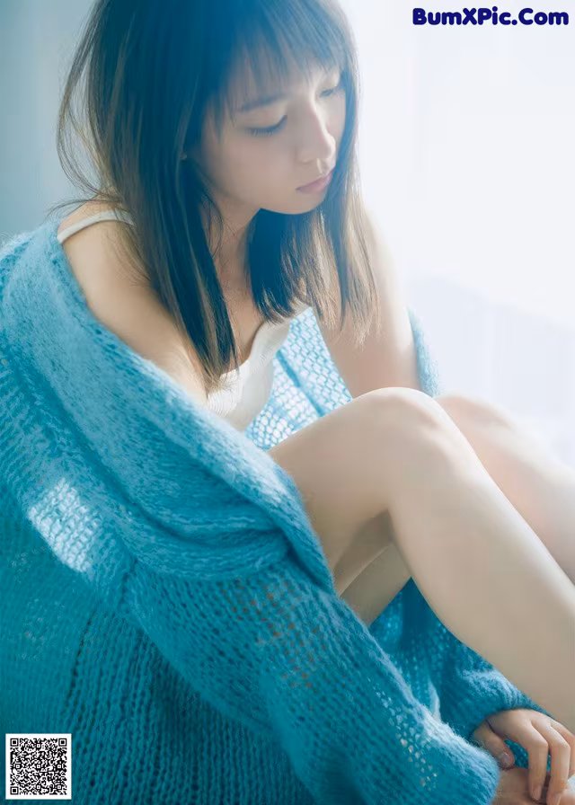 A woman sitting on a window sill wearing a blue sweater.