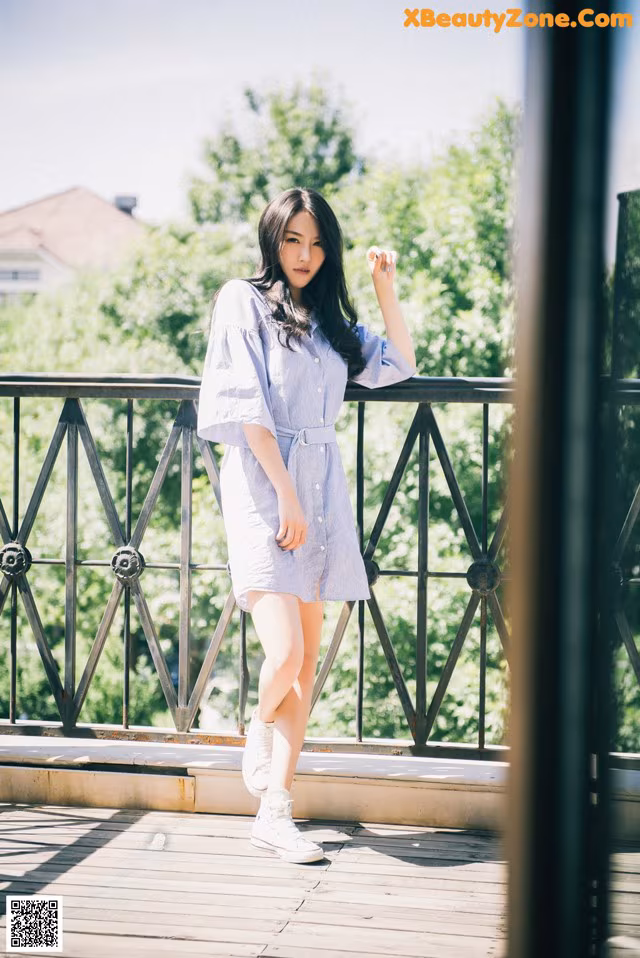 A woman in a blue and white dress standing on a balcony.