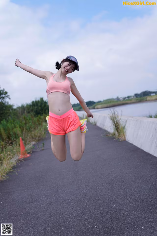 A woman in a pink sports bra top and pink shorts jumping in the air.