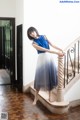 A woman in a blue top and a white skirt standing on a staircase.