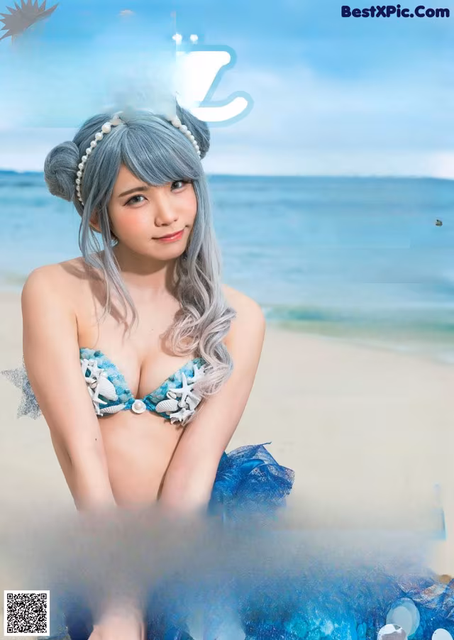 A woman in a blue dress sitting on a beach.