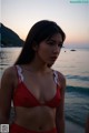 A woman in a red bikini standing on a beach.