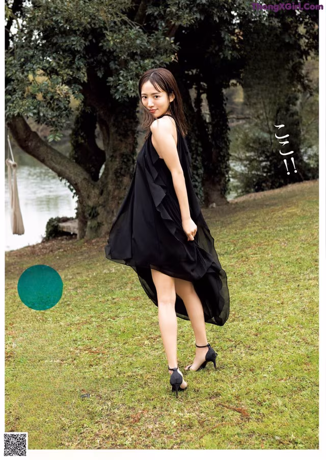 A woman in a black dress standing in the grass.
